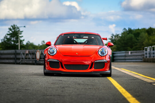 Red Porsche 911 sports car parked outside on an asphalt road. Front view of a fast racing car.