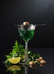 Glass of absinthe with ingredients on a black background.