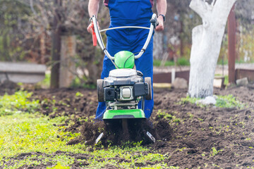 A farmer in the garden tills the land with a motorized cultivator or power tiller, preparing the soil for planting crops
