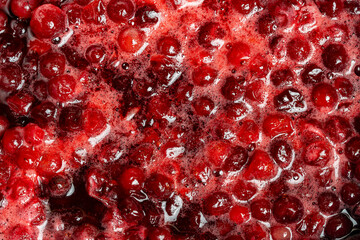 Red ripe cranberry in a saucepan during the preparation of a jam, closeup, top view