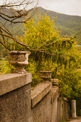 The fence is old concrete with a flowerpot on top. Autumn. Trees and mountains in the background