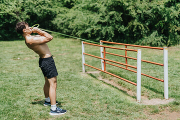 Fit man using resistance bands for exercise in a park. Highlighting outdoor fitness and strength training.