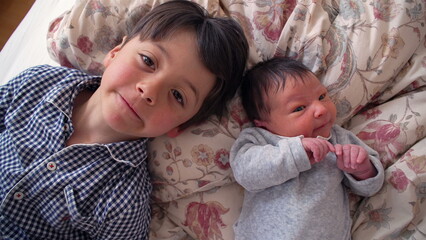 Young boy lying next to newborn sibling on a floral bed, illustrating the start of a lifelong bond...