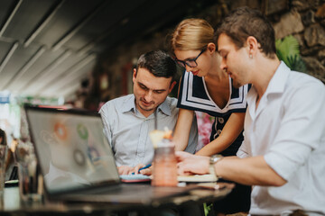 Three colleagues engage in a team meeting at a cafe, working together with a laptop and notes. Ideal for concepts of teamwork, collaboration, and informal business settings.