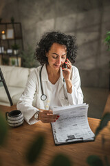 mature woman doctor read diagnosis from clipboard talk on mobile phone