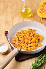 Preparing the filling for pumpkin ravioli or salad, fried pumpkin pieces in a light frying pan.