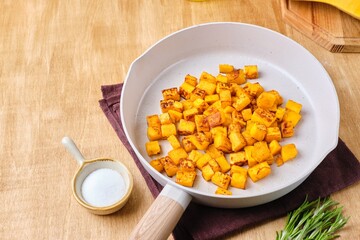 Preparing the filling for pumpkin ravioli or salad, fried pumpkin pieces in a light frying pan.