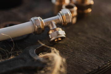 Brass plumbing fittings and PEX pipe fittings lying on an old wooden countertop, next to a tool, plumbing wrenches (selective focus)