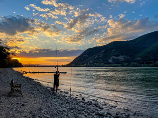 A Man Is Fishing On Danube In Summer During A Sunset