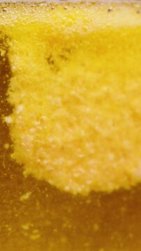 Vertical video. A partially dissolved Effervescent Tablet disperses, forming a cloudy, bubbling pattern in a Yellow Liquid. Slow Motion