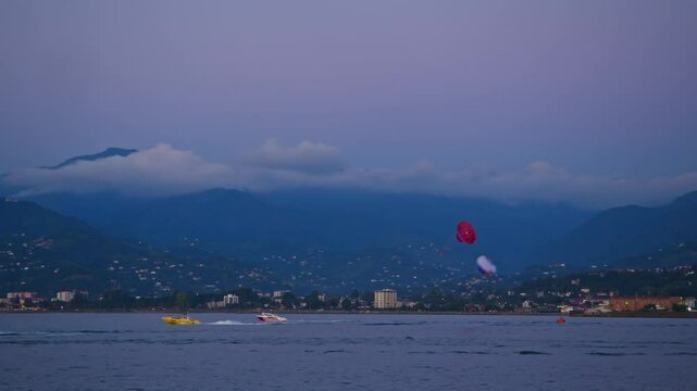 A seascape of several tourists parasailing in Batumi's picturesque bay in Georgia in the evening. Slow motion