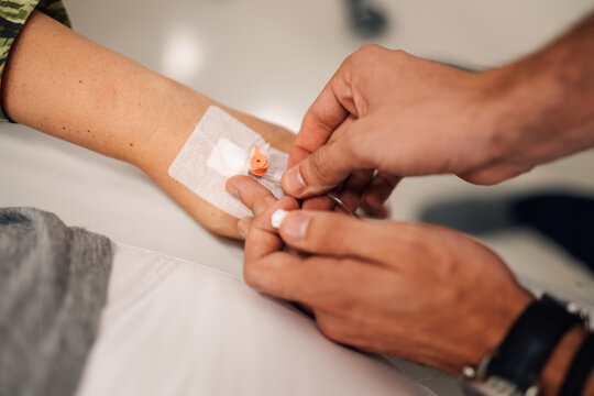 Healthcare professional inserting IV catheter into patient&rsquo;s arm.
