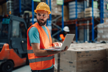 Warehouse worker inputting data on laptop for inventory management.