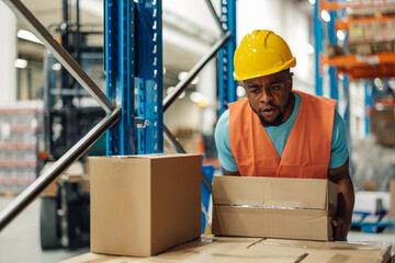 Dedicated african american male worker carrying cardboard box in warehouse.
