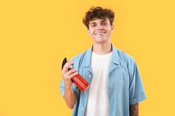 Handsome young man with bottle of hair spray on yellow background