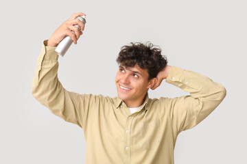 Handsome young man applying hair spray on his curly hair against grey background