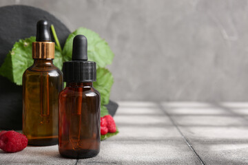 Bottles of cosmetic raspberry oil on grey tile table