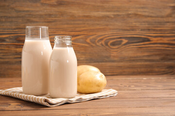 Bottles of tasty potato milk on wooden background