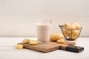 Glass of tasty potato milk on white wooden background