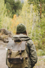 A young woman walks through the forest with a backpack on her back. rear view. during his journey. Travel and fashion concept.