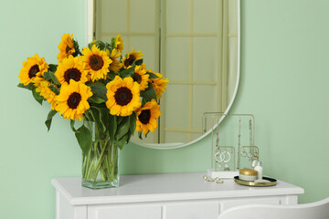 Vase with beautiful sunflowers on dressing table near green wall