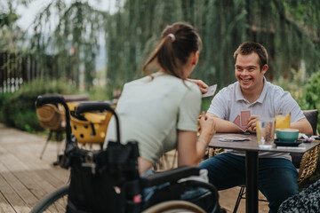 A joyful moment between friends playing cards outside. One friend uses a wheelchair, highlighting inclusivity and fun in nature. Ideal for concepts of friendship and accessibility.