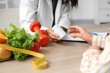 Female nutritionist giving pill bottle to patient in office, closeup