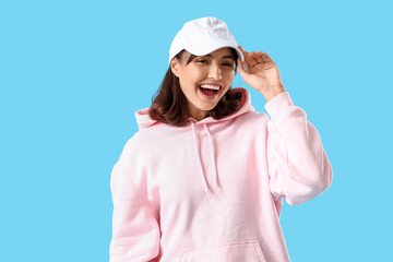 Young woman in cap and pink hoodie on blue background