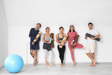 Naklejka premium Group of sporty young people with yoga mats and water bottles in gym