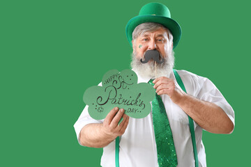 Mature man with paper mustache and card on green background. St. Patrick's Day celebration