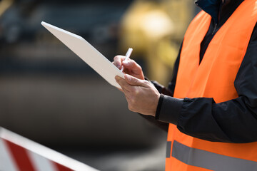 Construction site supervisor taking notes while wearing safety gear and overseeing project progress during daylight hours