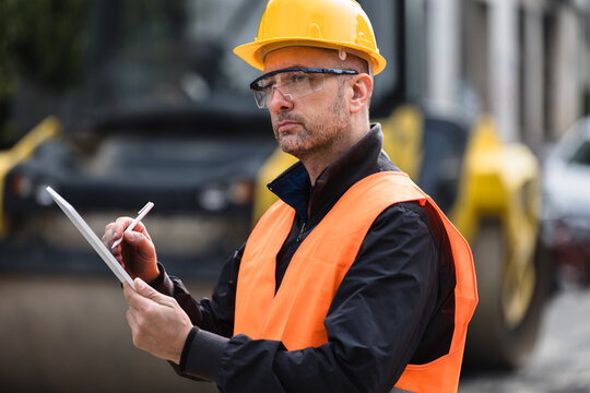 Construction site supervisor reviewing plans while wearing safety gear outdoors during daytime