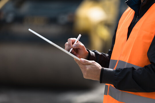 Construction worker in safety vest taking notes at a job site during daylight hours