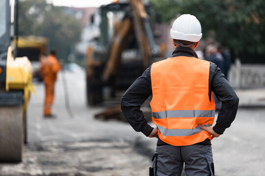 Construction worker observes roadwork activities at a busy urban site during day time