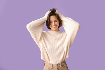 Happy young woman in stylish white sweater on lilac background