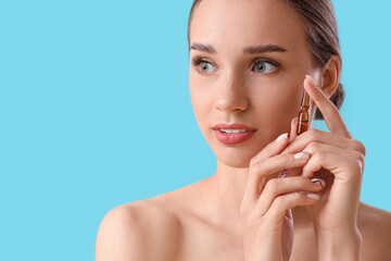 Beautiful young woman with ampoule on blue background, closeup