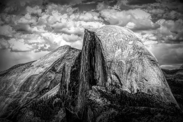 Dramatic black and white capture of Half Dome from Glacier Point in Yosemite National Park. The iconic granite monolith towers against a cloudy sky, showcasing nature's raw power and beauty. © John