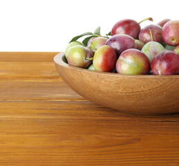 Fresh plums and green leaves in bowl on wooden table against white background