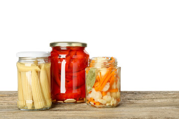 Different pickled products in jars on wooden table against white background