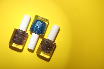 Nail polishes in bottles on yellow background, flat lay. Space for text