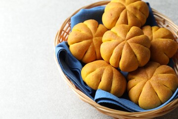 Wicker basket with tasty pumpkin shaped buns on light table, closeup. Space for text