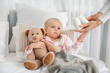 Little girl ill with chickenpox taking pills from her mother in bedroom