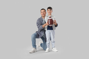 Cute little boy with rugby ball and his father on light background