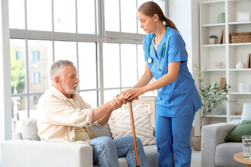 Senior man suffering from Parkinson syndrome with stick and nurse at home