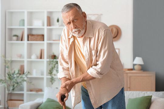 Senior man suffering from Parkinson syndrome with stick at home