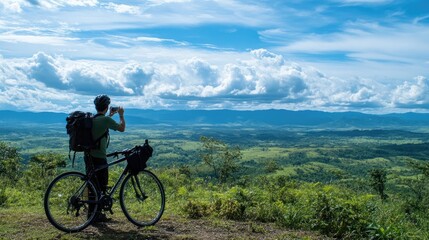 A cyclist stopping to take a photo of the scenic view from a hilltop, with a camera in hand and the bicycle leaning nearby, overlooking a vast landscape.