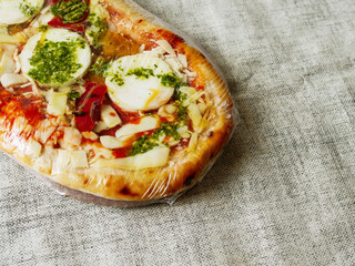 Oval shape pizza with mozzarella cheese, spinach and red peppers on a simple table cloth. Popular Italian style meal with premium high quality ingredients. Uncooked product. Fine fast food.