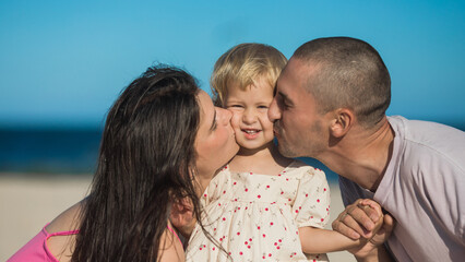 Happy family  at the ocean.  Parents kiss  her daughter