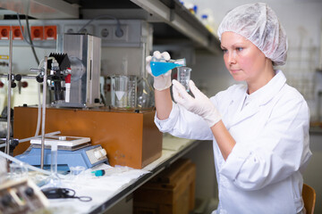 Middle-aged female scientist making research pouring blue reagent into test tubes working in modern...