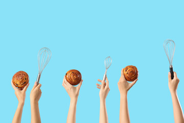 Female hands with tasty buns and whisks on blue background